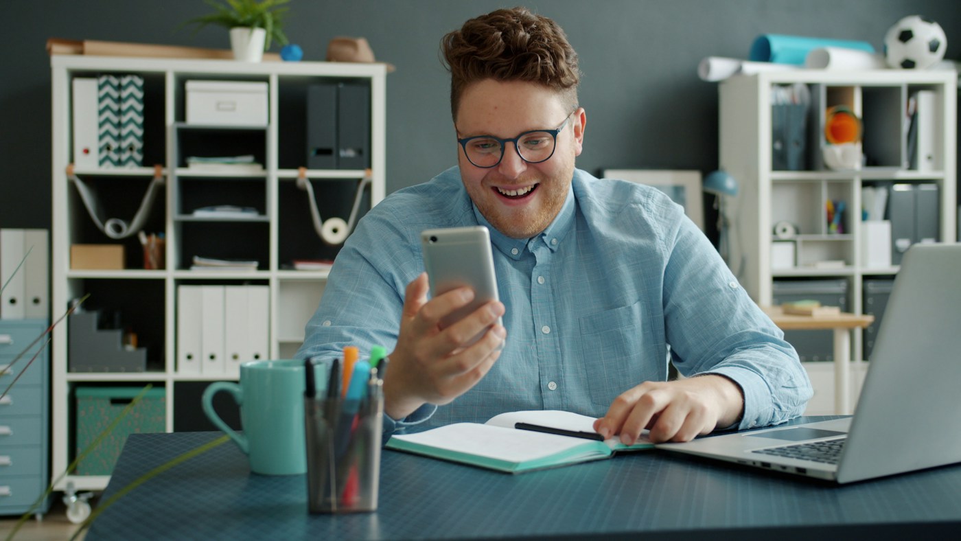 A business owner at his desk laughing with delight as he looks at his phone