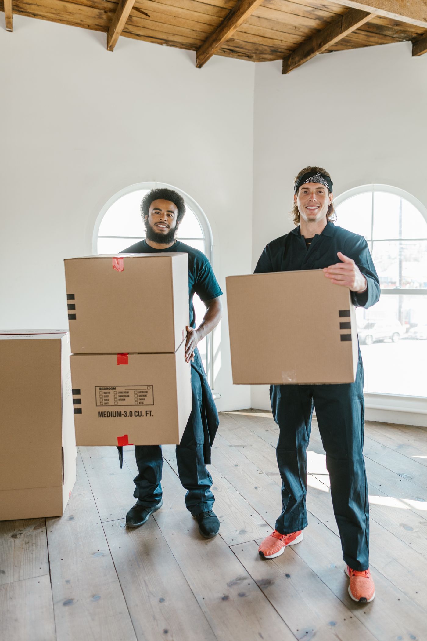 Two smiling removalists carrying cardboard boxes through an empty room