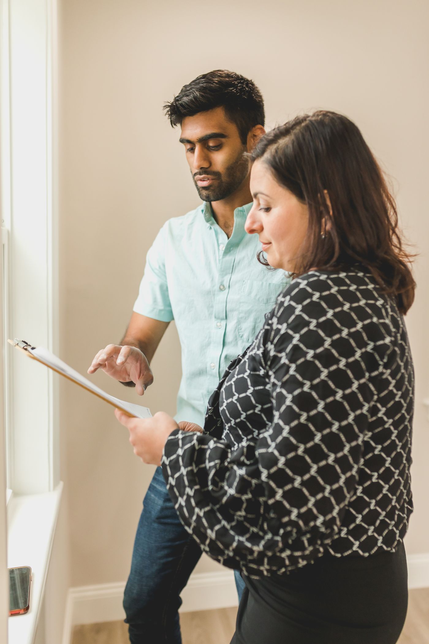 Two people going through a checklist on a clipboard together, standing by a window